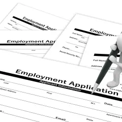 Biała figurka pisze długopisem na formularzu "Employment Application". To dokumenty do wypełnienia po angielsku.